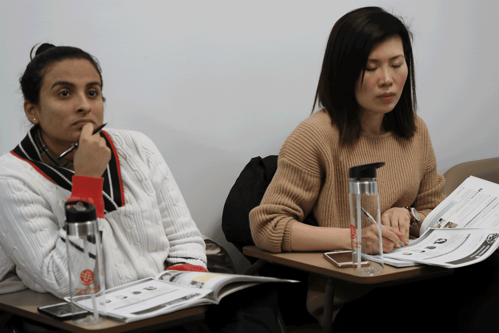 Two women studying at desks, working on papers and having water bottles nearby.