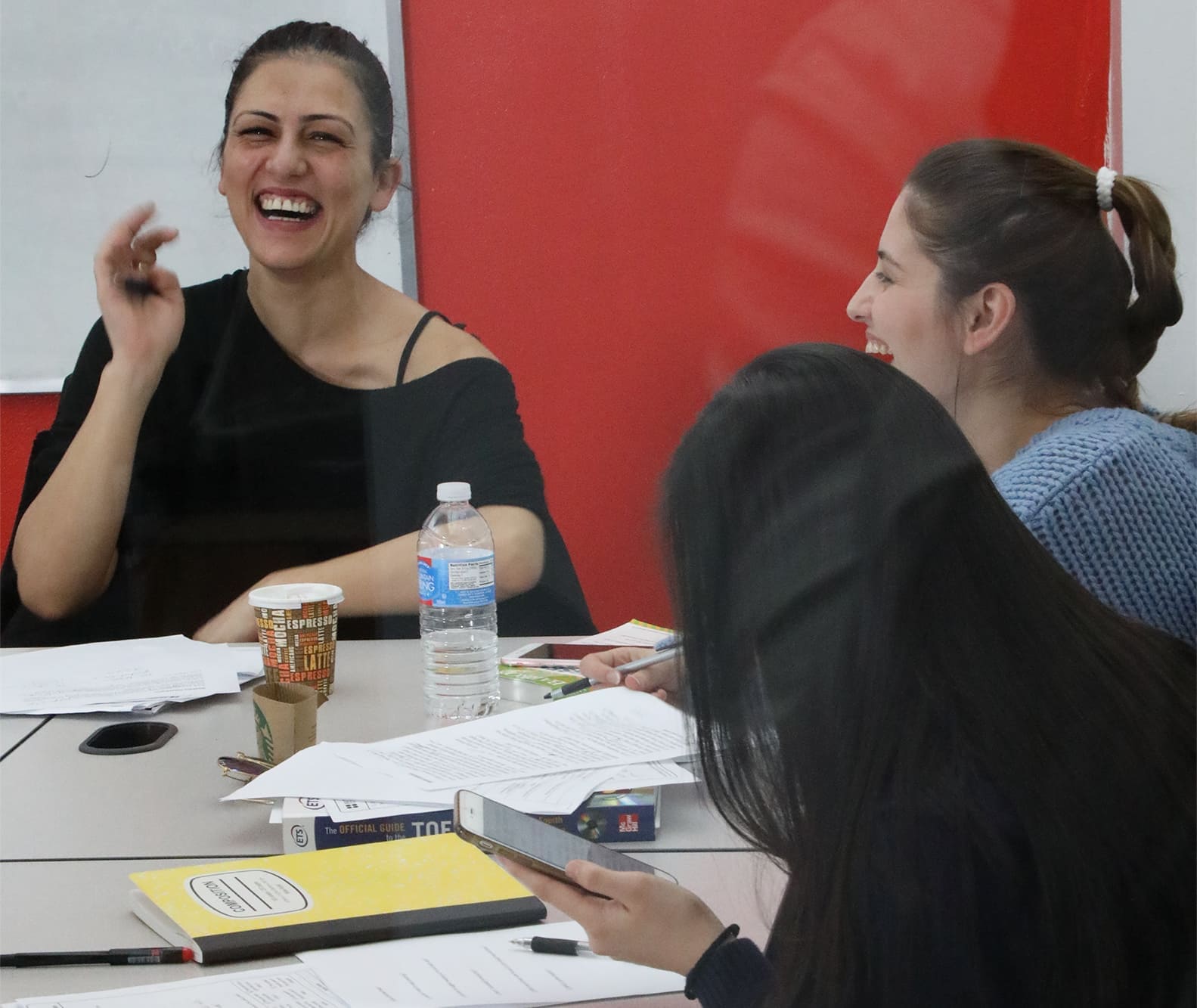 Women at New York English Center sit around a table, laughing together.